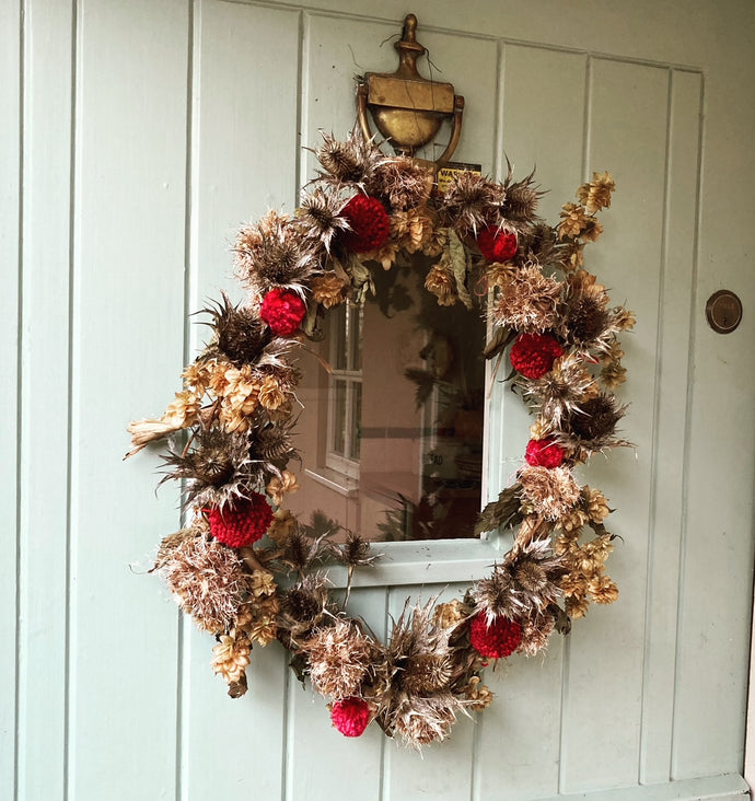 A wreath made with natural foliage is simple decorated with a few small red pompoms.