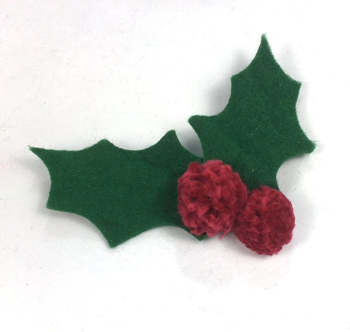 Simple Christmas holly decorations are made by cutting holly leaf shapes from green felt and stitching through them with red pompom 'berries' These could be made into handmade cards or a simple decoration for a present.