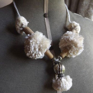 This necklace is made by threading wooden beads and tying pompoms onto a hand made cord. Try using some of the yarn out of the Deluxe or Braid Making Kits to create these pompoms.