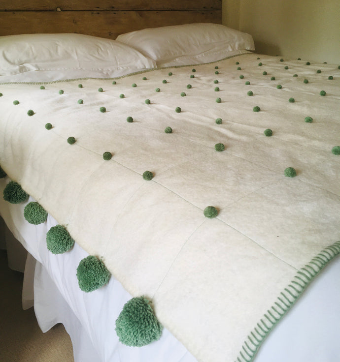 Lots of little green cotton pompoms decorate this blanket.